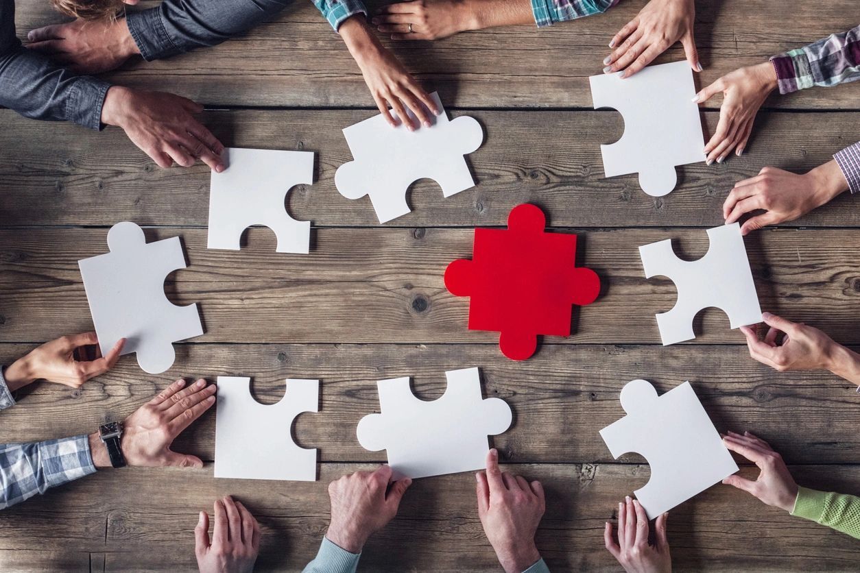 A group of people sitting around a table with white puzzle pieces.